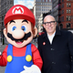 A person wearing a Mario mascot outfit stands next to Nintendo president Doug Bowser smiling at the camera in a backdrop of Manhattan